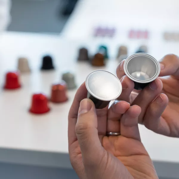 AluSense team member inspecting empty aluminium coffee capsules by hand, with a wide range of coloured capsules visible in the background.
