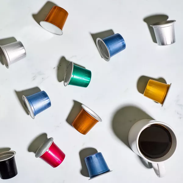 AluSense InfinityCup aluminium Keurig® compatible coffee pods in multiple colours displayed alongside a freshly brewed cup of coffee.