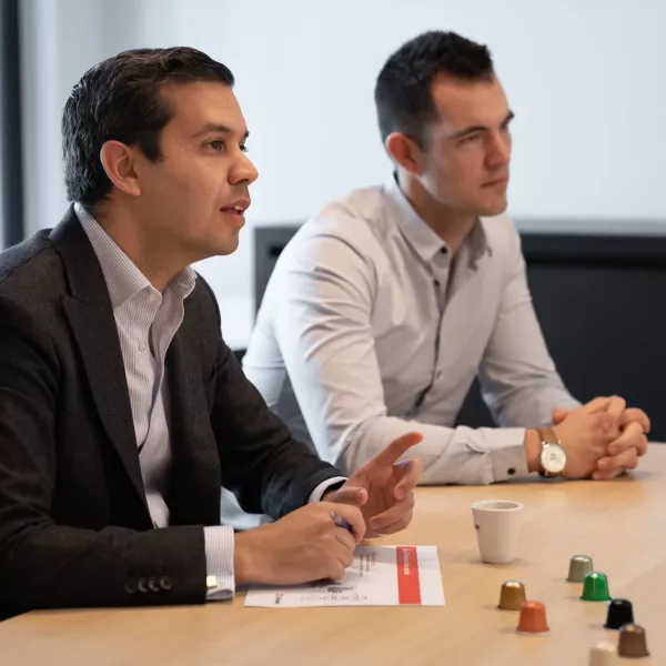 AluSense team members in a business meeting discussing long-term partnerships, with a range of coloured aluminium coffee capsules on the table.