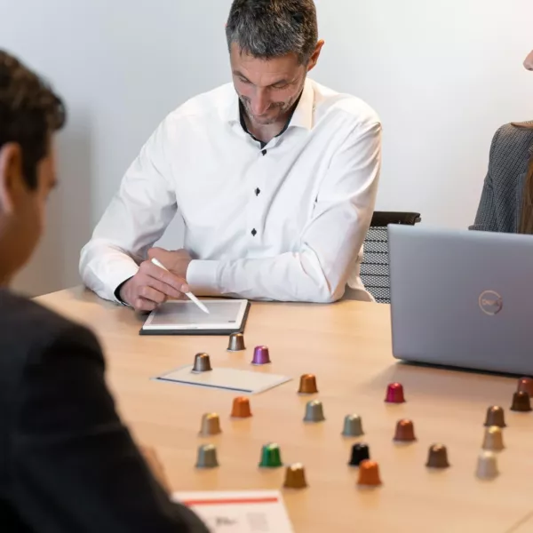 AluSense expert consulting with a client about their coffee capsule project, with a range of coloured aluminium capsules displayed on the table.